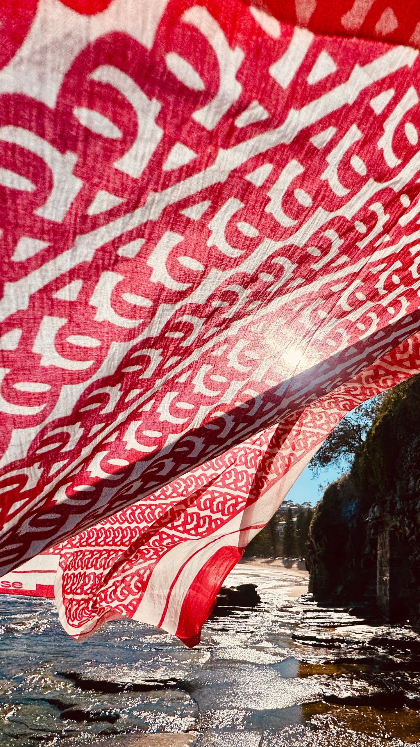 Red and white patterned fabric draped over a natural landscape with water and trees.