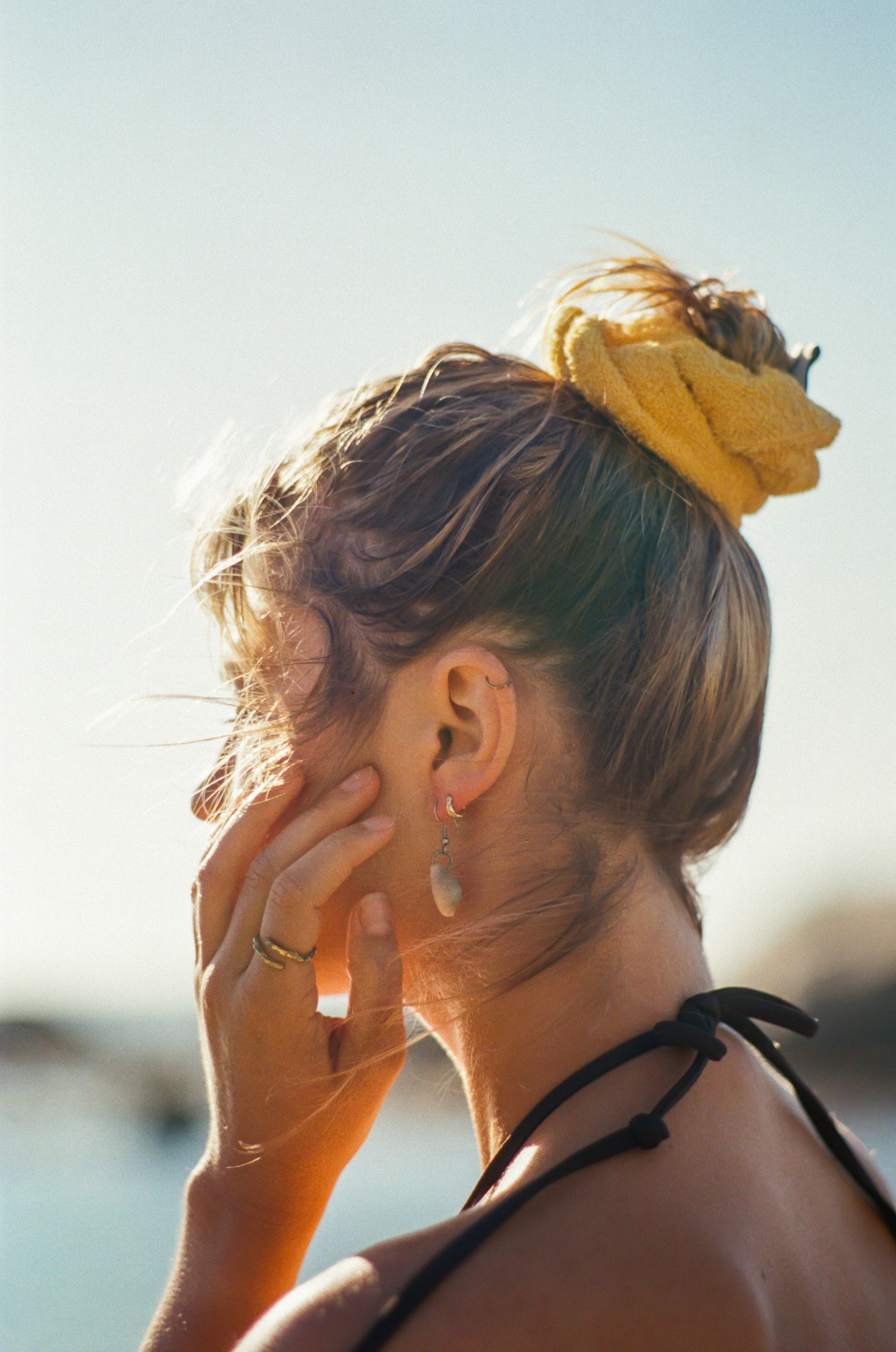 Woman with a yellow hair scrunchie and black swim strap over shoulder against a blurred beach background