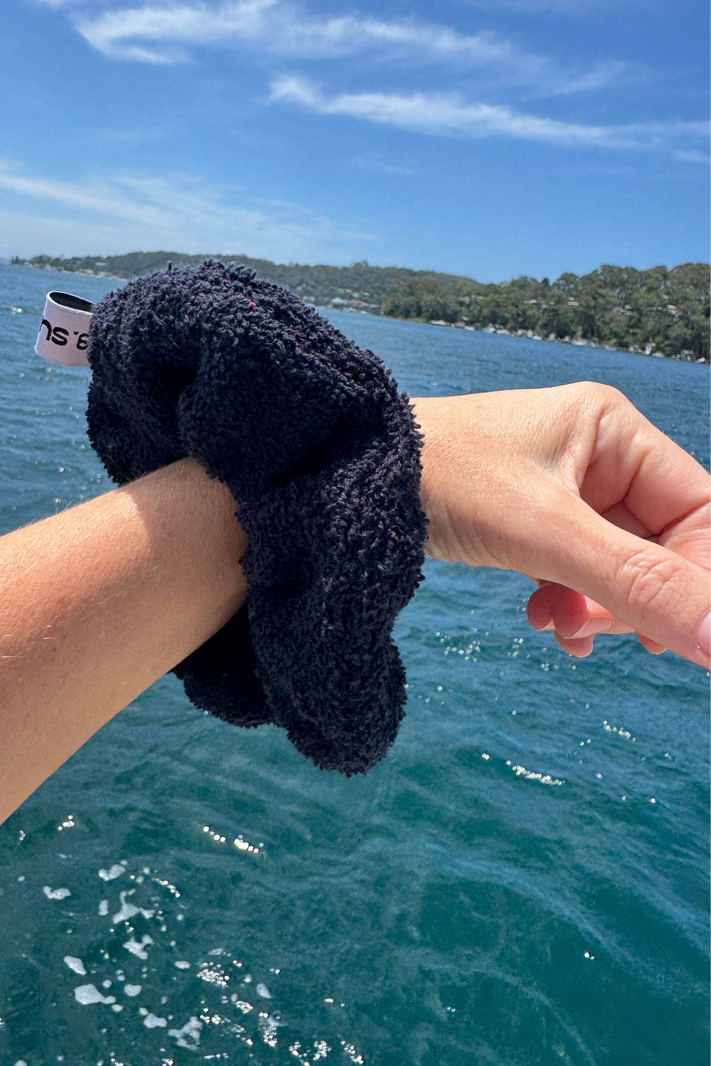 Person holding a black towelling scrunchie with a white label over a body of water