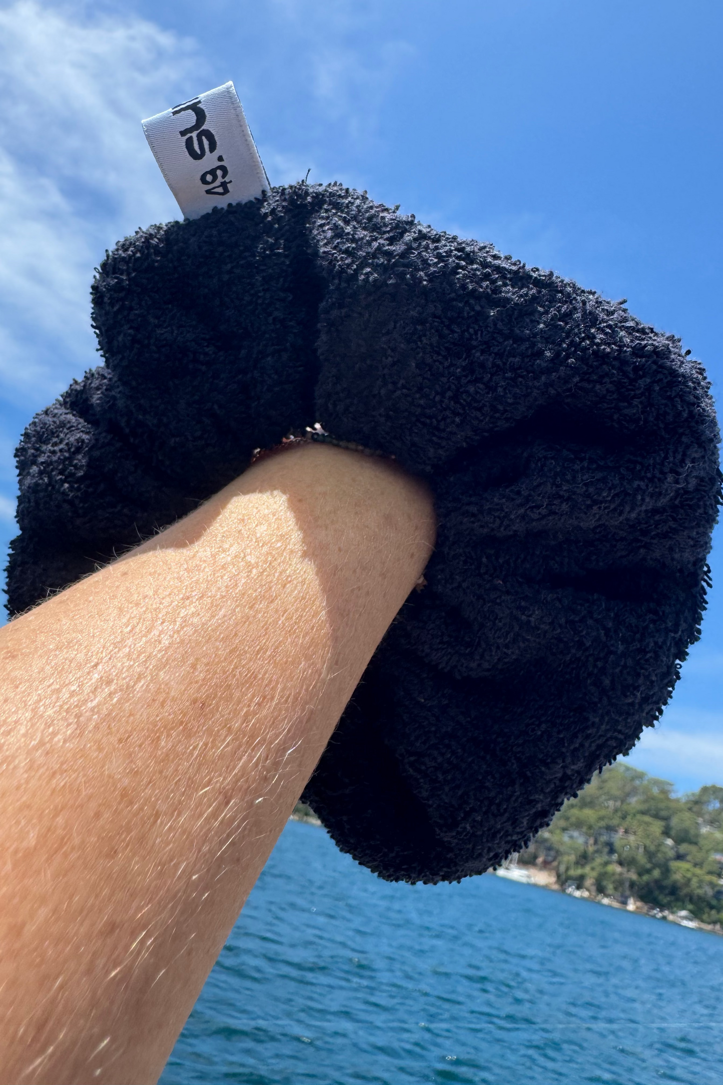 Black fuzzy scrunchie held by a hand with a scenic background of water and sky.