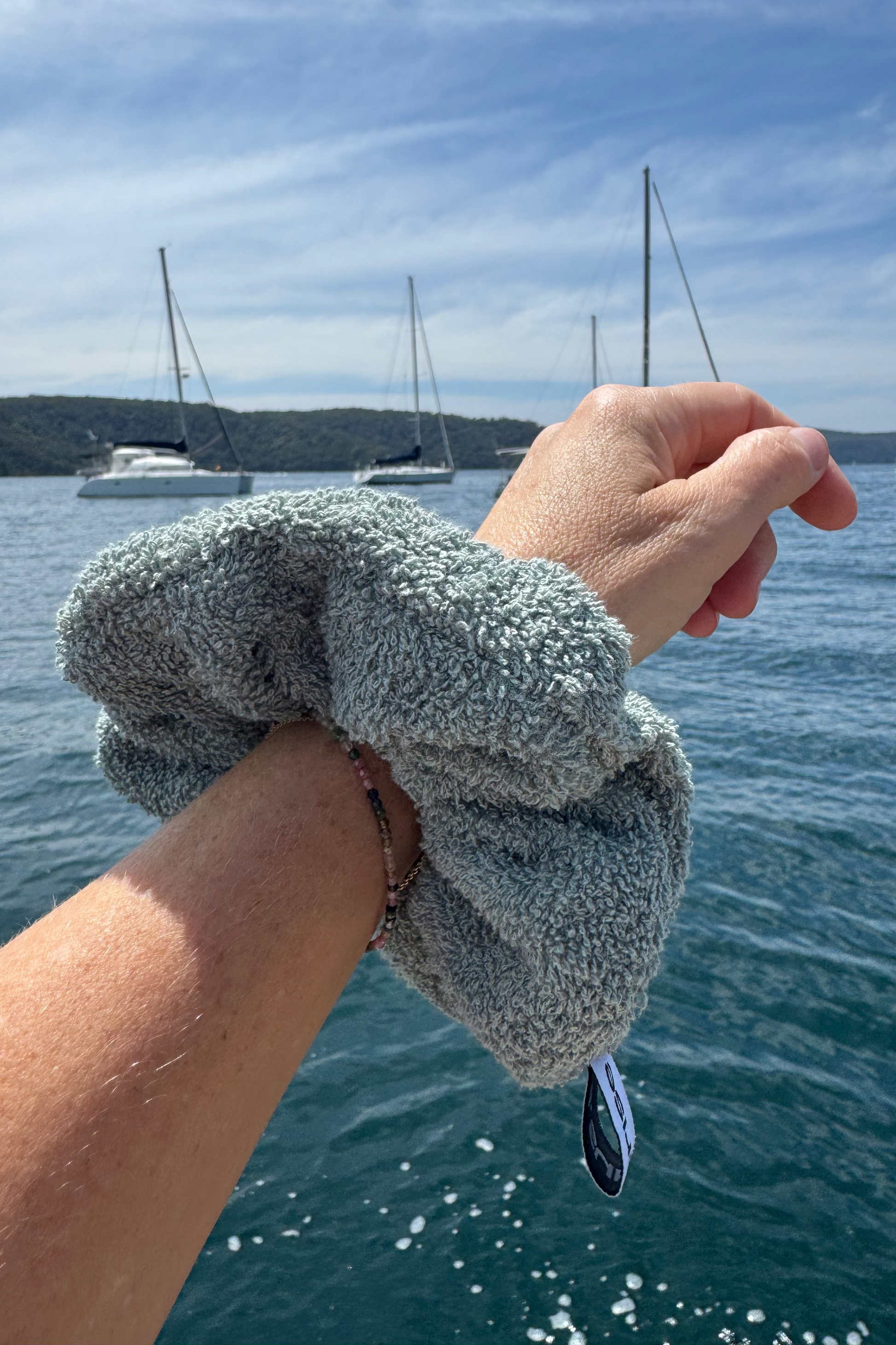 Hand wearing a green scrunchie with a scenic background of boats on water.