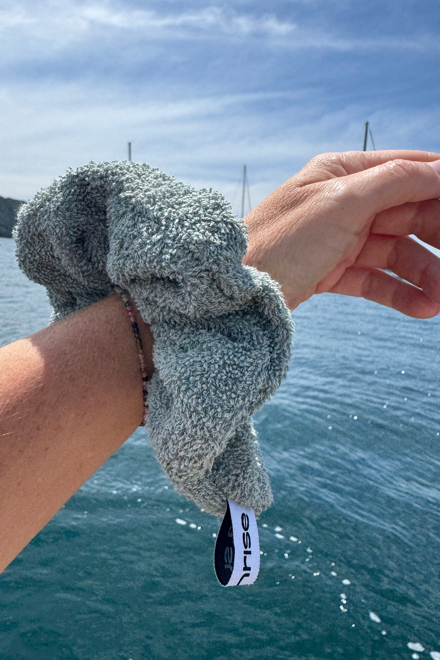Person holding a textured green scrunchie with a tag against a blue water background