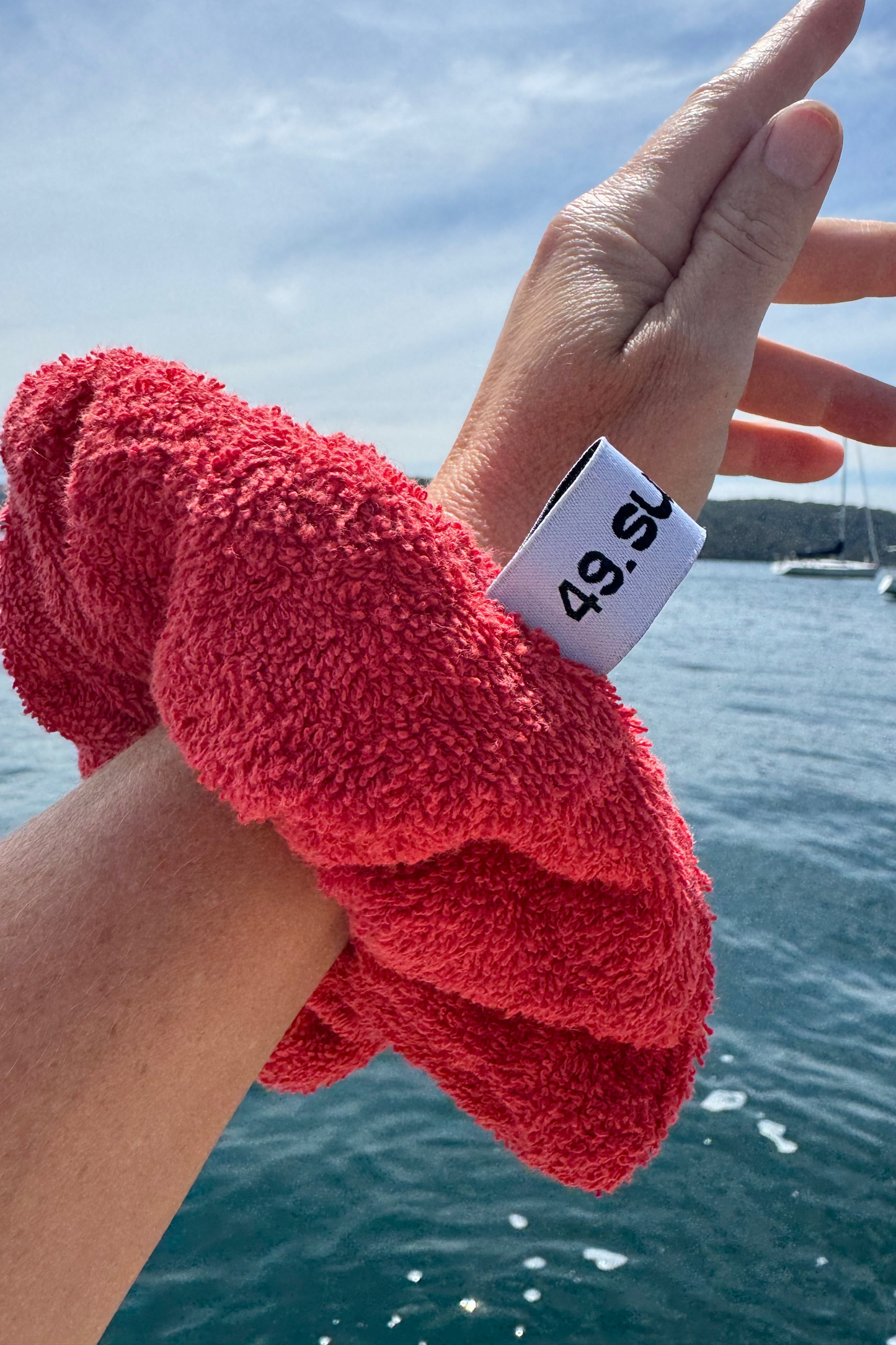 Hand wearing a red towel with a weight label against a blue water and sky background