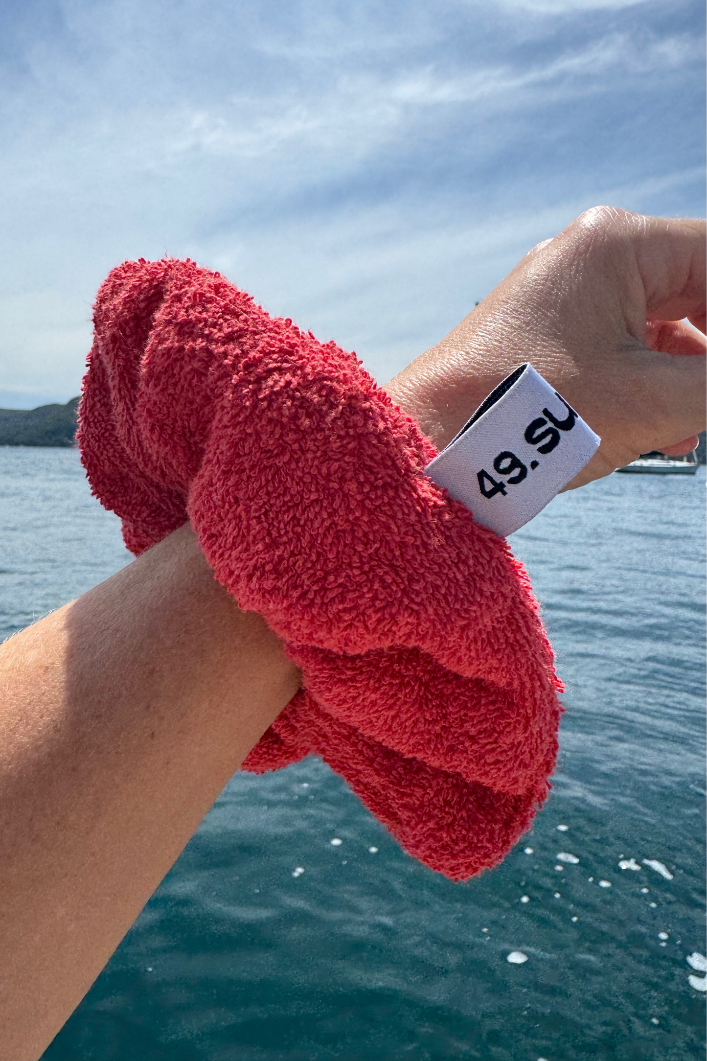 Person holding a red towel with a scenic background of water and sky.