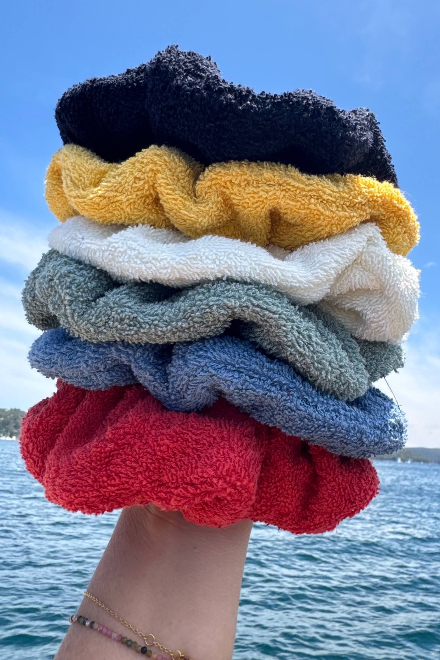 Stack of colorful scrunchies held against a blue sky and water background