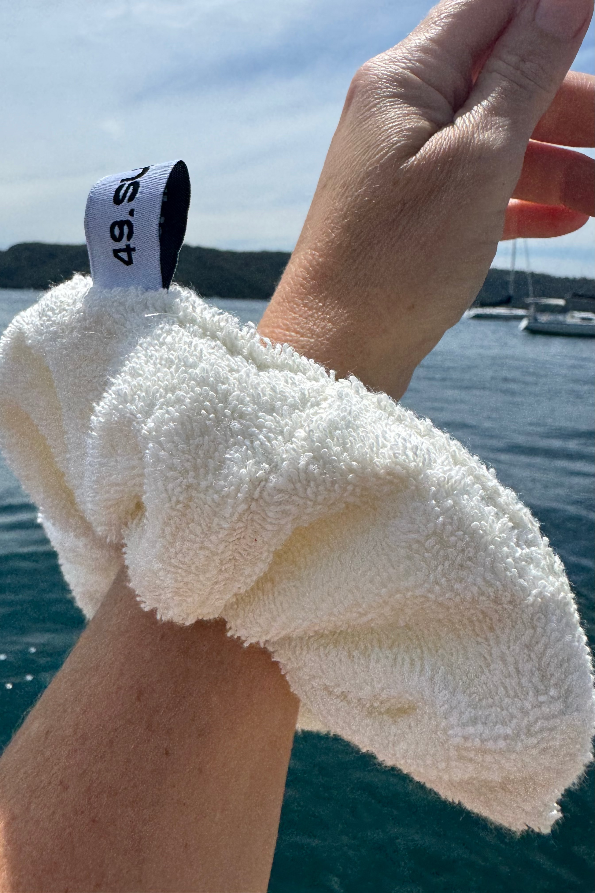 Hand holding a white towelling scrunchie with a blue sky and water in the background