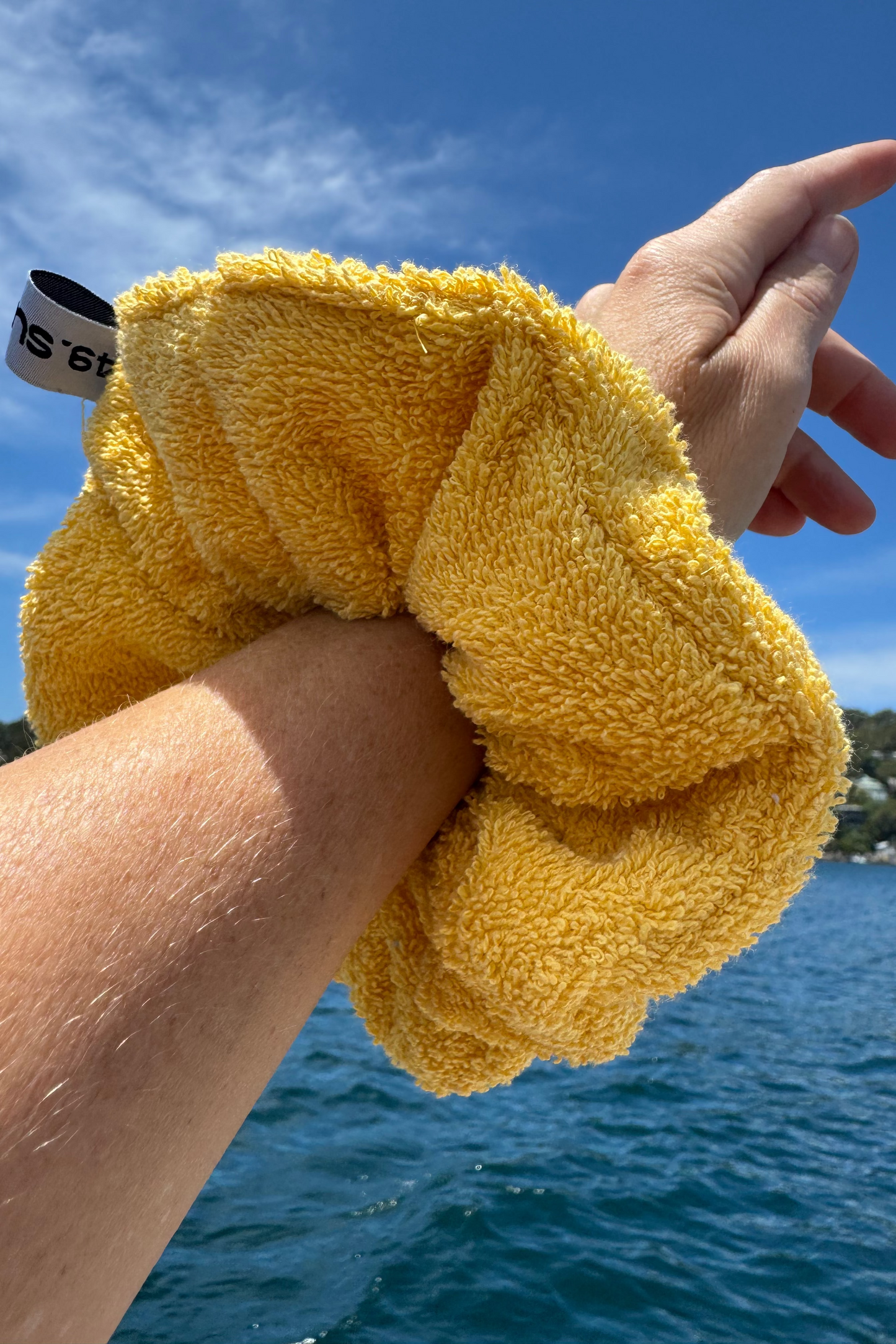 Yellow towelling scrunchie held by a person with a blue sky and water background