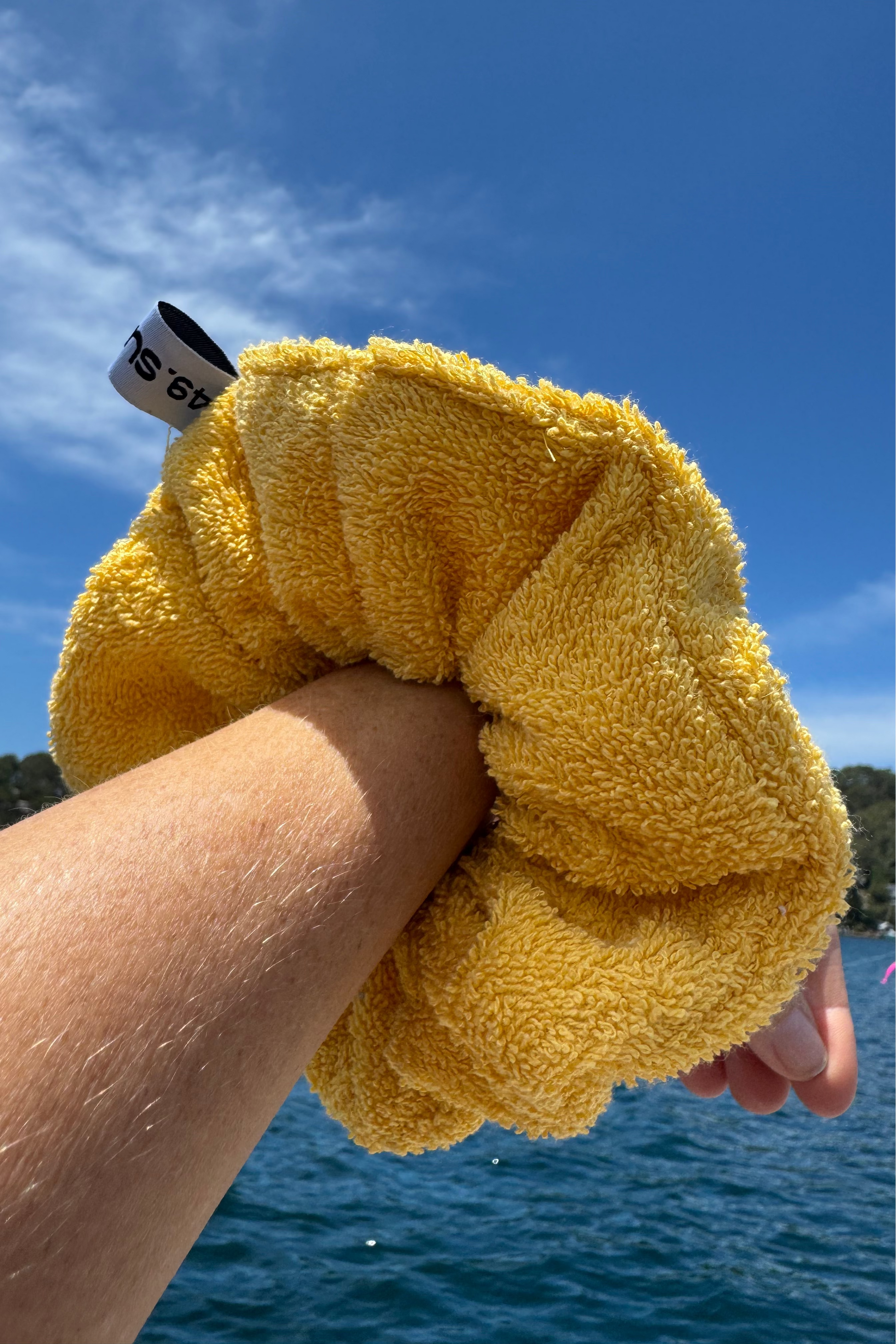 Yellow scrunchie held by a hand with a blue sky and water background